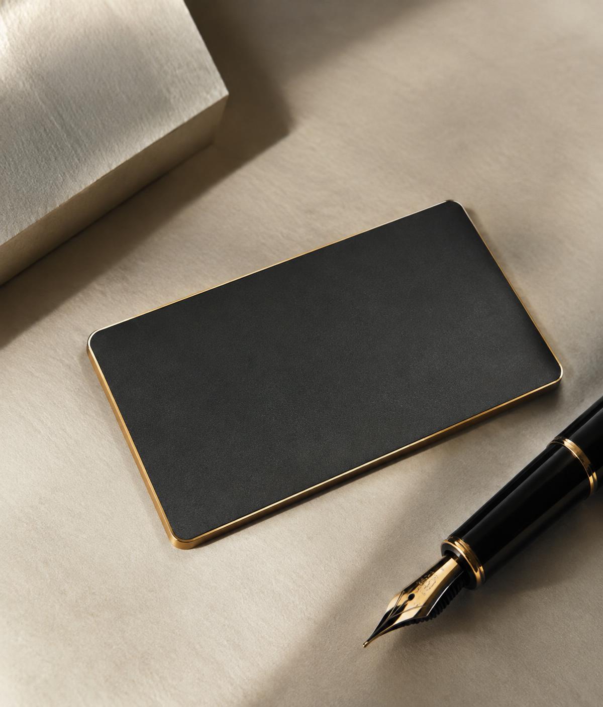 A charcoal card with a gold edge beside a fountain pen on ivory paper